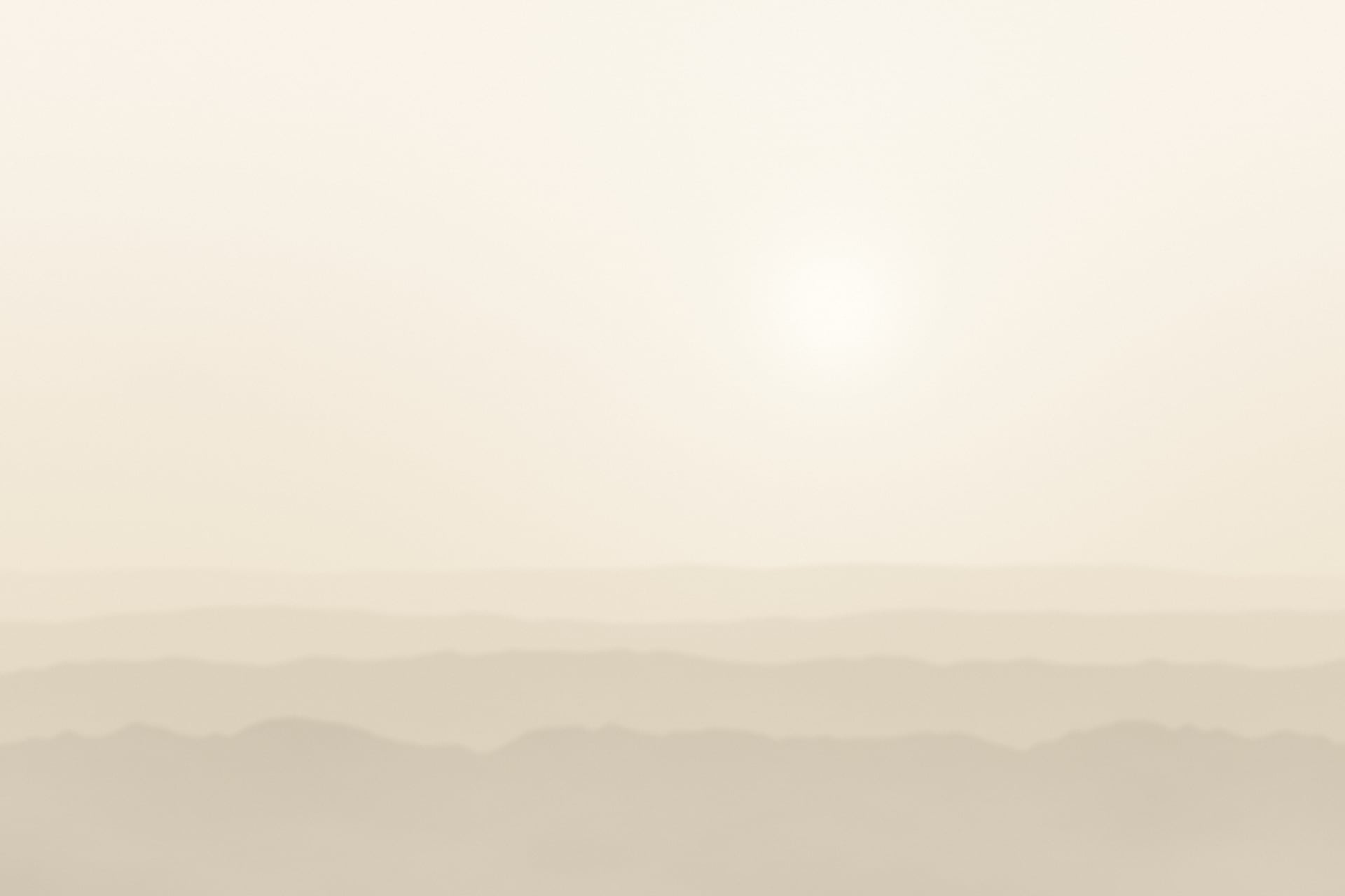 Hazy ridgelines dissolving into pale morning fog beneath a veiled sun